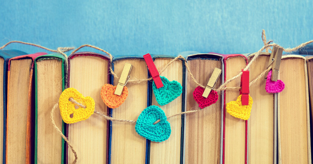 Many multicolor crochet hearts on books over blue background.