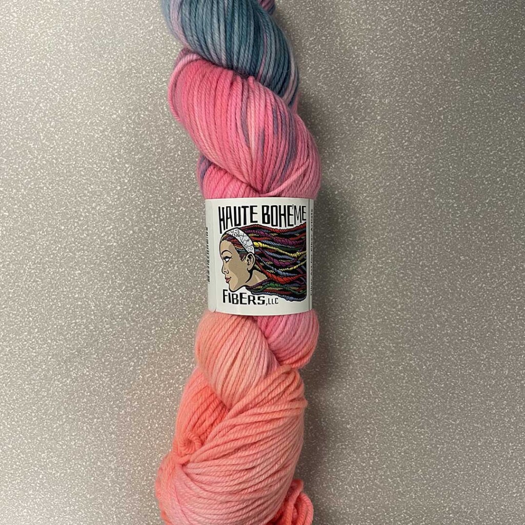 A neon variegated skein of Haute Boheme Fibers yarn in shades of hot pink, bright orange, peach, and dusty blue.